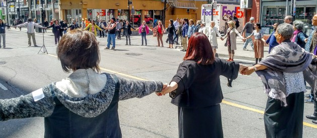 People holding hands and standing in a circle in the middle of the road 