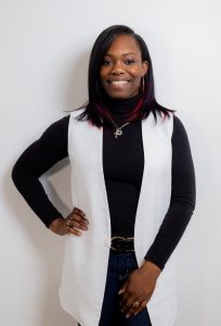 A women smelling wearing black sweater and white sleeveless cardigan